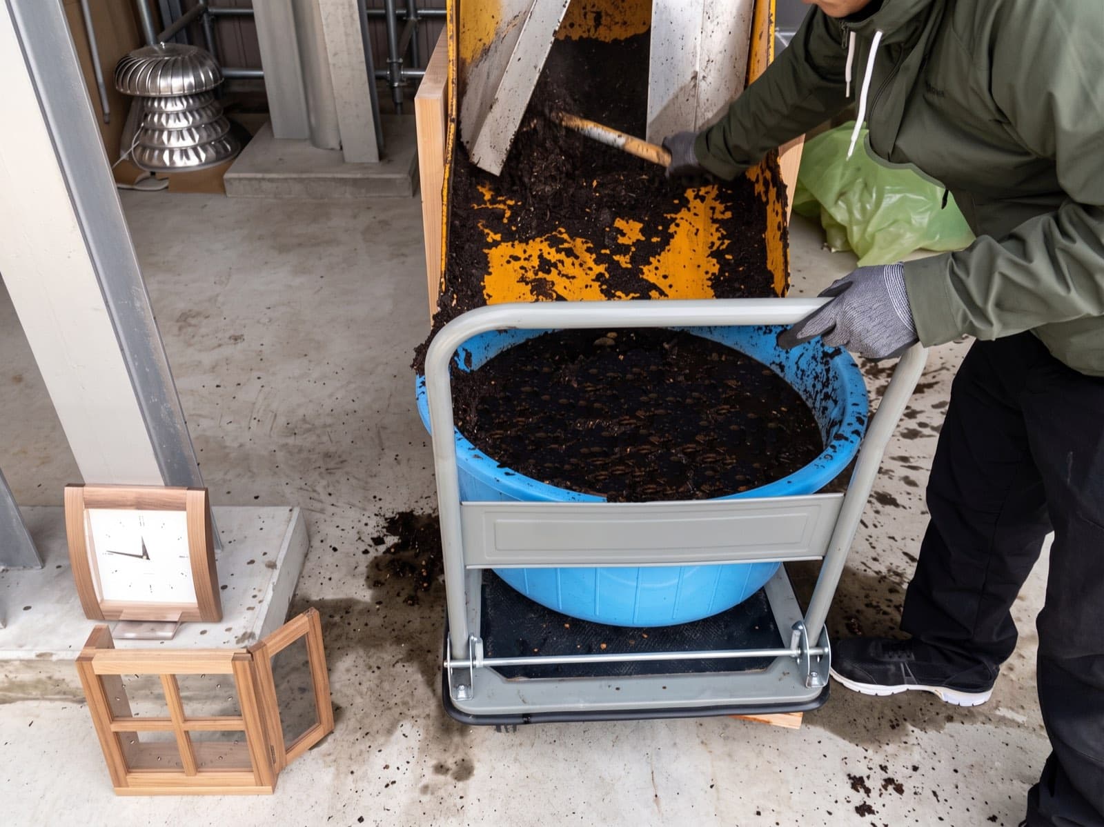Overhead view of dark granular processed output discharging into a blue tub, with pale woody bark fragments visible in the material — the treated cellulosic residue after subcritical water processing.